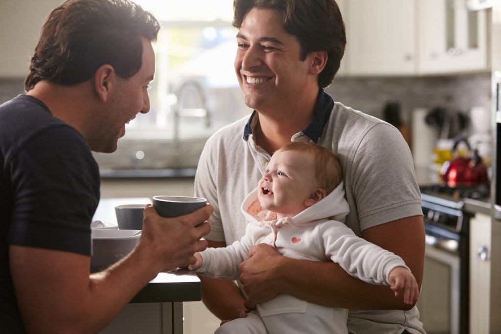 Male gay couple holding baby girl in their kitchen Male gay couple holding baby girl in their kitchen.