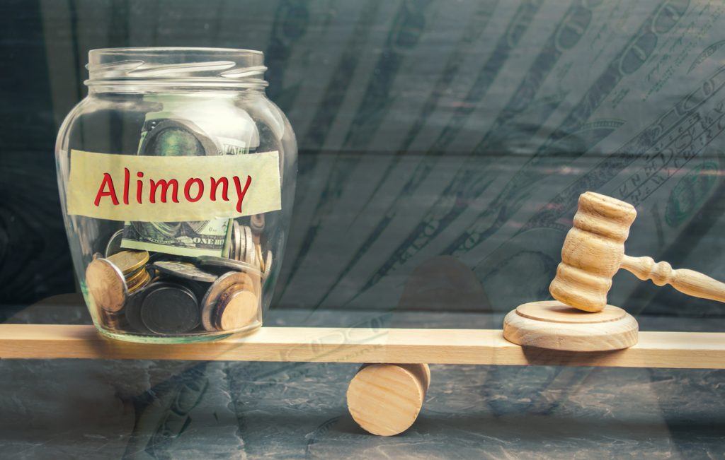 Glass jar and the inscription "Alimony" and the hammer of the judge are on the scales. Payment of alimony of one of the spouses. Debt. Child custody. Judgment. Justice. Divorce. Court North Carolina Wife Ordered to Pay Alimony to Husband